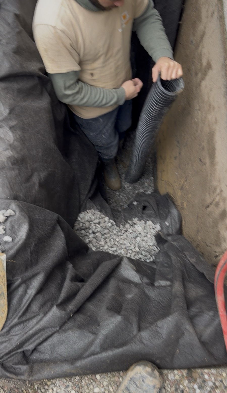 Crew installing drain pipe with filter fabric and stone