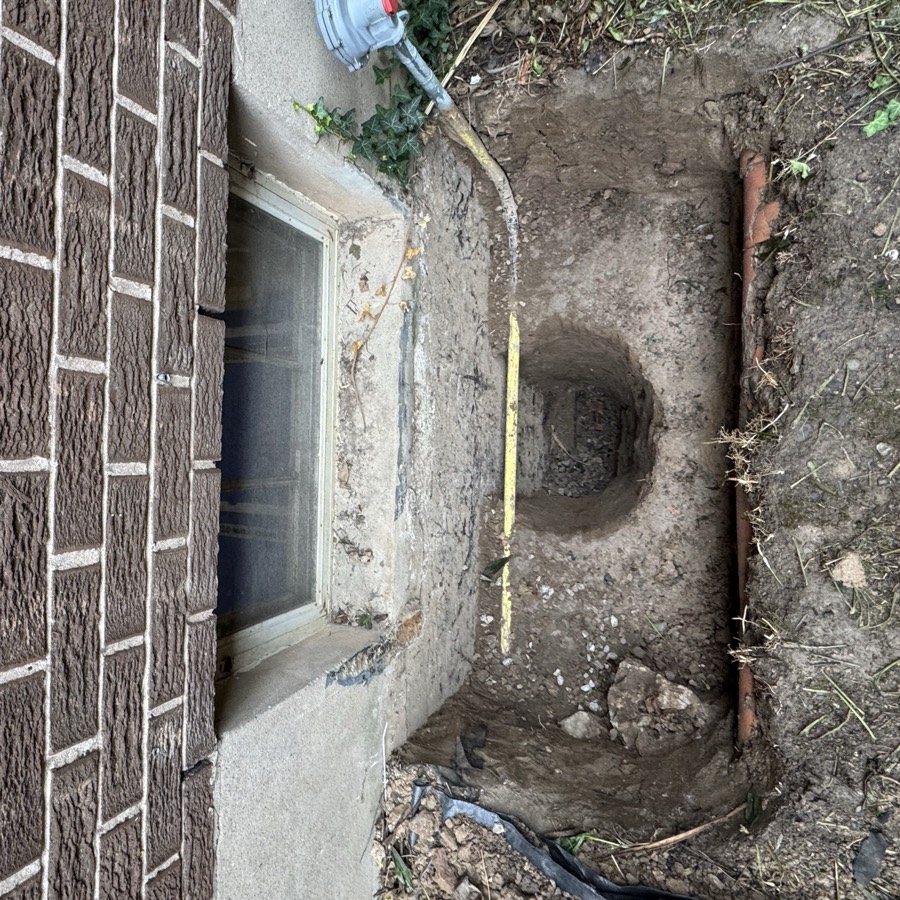 Window well hand dug cleanly beside a marked gas line under a basement window