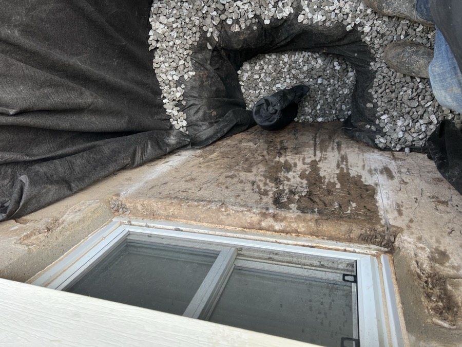 Finished window well drainage stone bed with filter fabric and drain sock