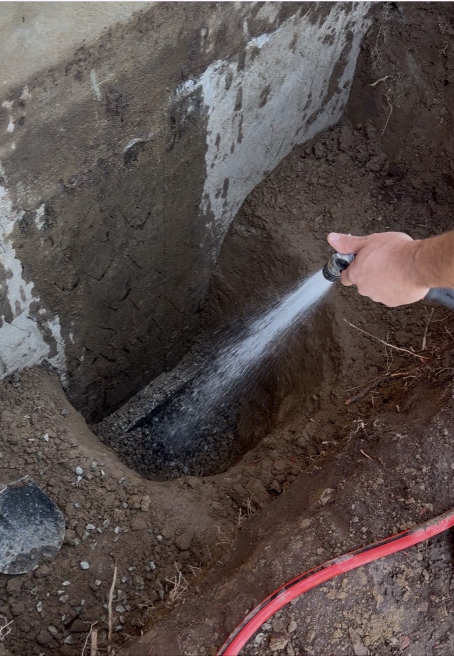 Window well drainage tested with a running hose on the new stone bed before backfilling