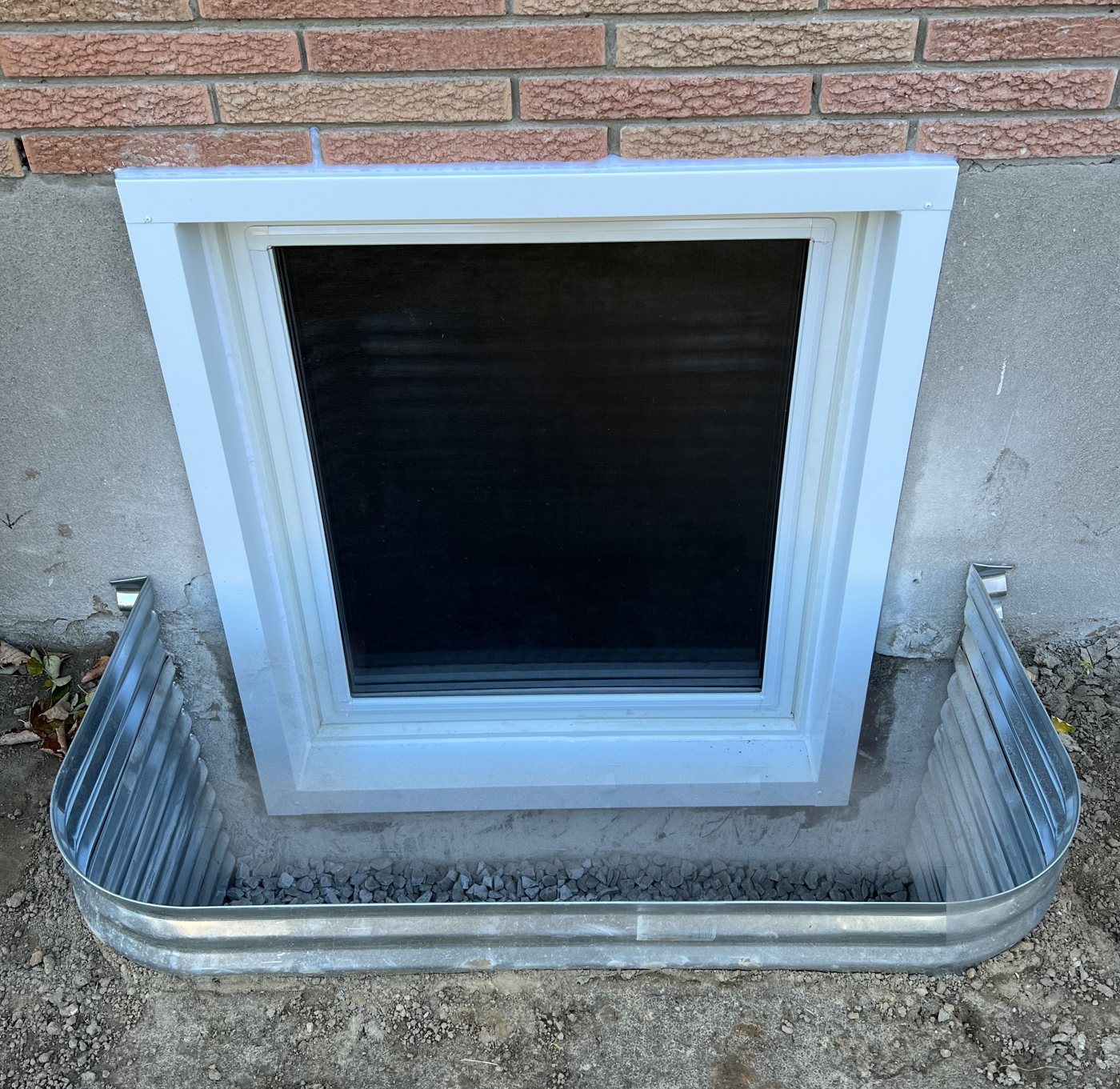 Egress window installed in a galvanized steel well over a drainage stone bed